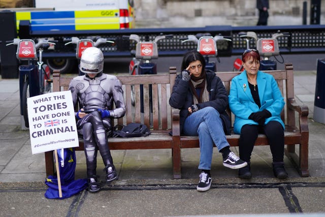 A protester dressed as RoboCop sits on a bench near the Palace of Westminster, as the Chancellor delivers his Budget to Parliament