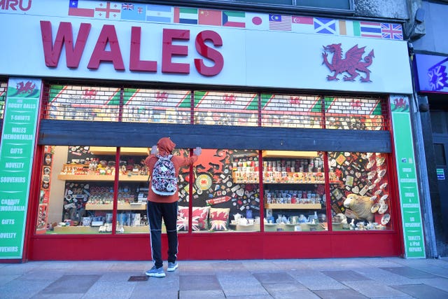 A shop owner pulls the shutters down on the Wales souvenir shop in Cardiff city centre before the 'firebreak' lockdown