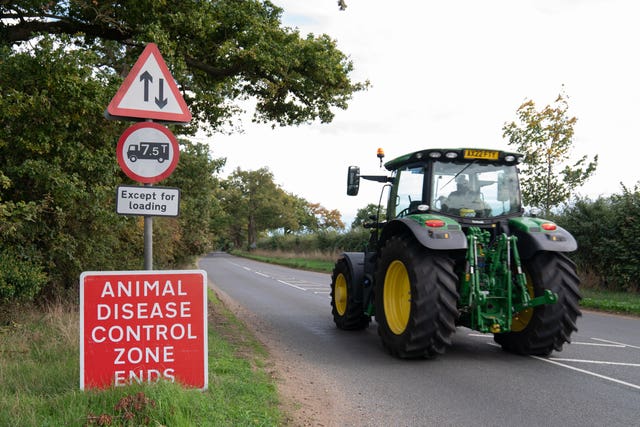 tractor drives past a sign that says 'animal disease control zone'
