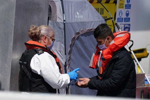 A man is given hand sanitiser by a Border Force officer as a group of people thought to be migrants are brought in to Dover, Kent, on board a Border Force vessel, following a small boat incident in the Channel