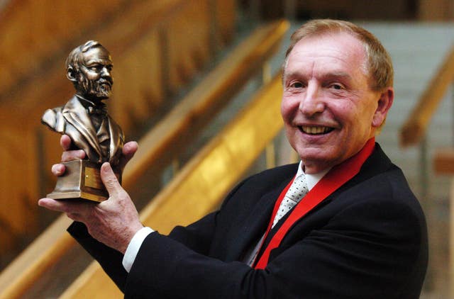 Sir Tom Farmer smiling while holding up award
