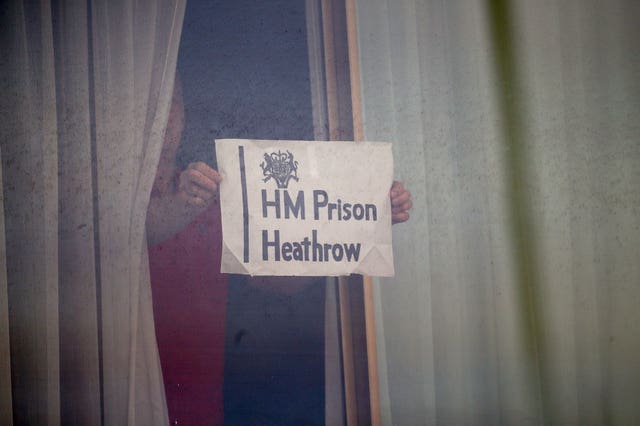 A man holds a sign against a window at the Renaissance London Heathrow Hotel during quarantine 