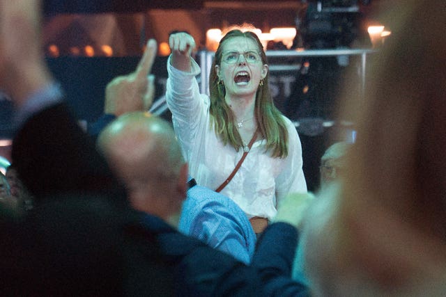 A demonstrator shouts while Reform UK leader Nigel Farage delivers a keynote speech