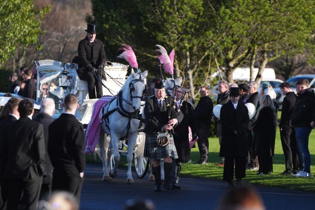 A piper plays while leading a white horse-drawn hearse