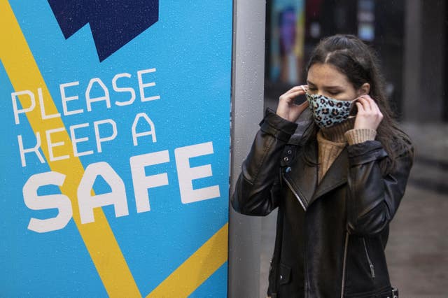 A young woman in Belfast puts on her face covering as she walks past a Covid-19 safety message from Belfast City Council