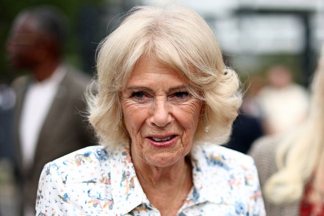 Queen Camilla smiling wearing a white floral shirt dress