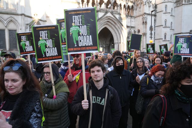A group of people holding up signs reading 'Free Mo Chara' outside a court building