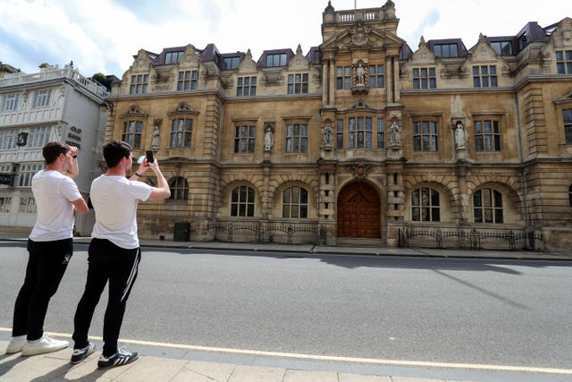 Passers-by photograph the Rhodes statue at Oriel College