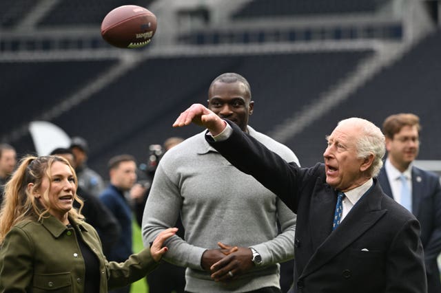 The King launches an American football in the air as he taught how to do so during a visit to Tottenham Hotspur Stadium on Wednesday