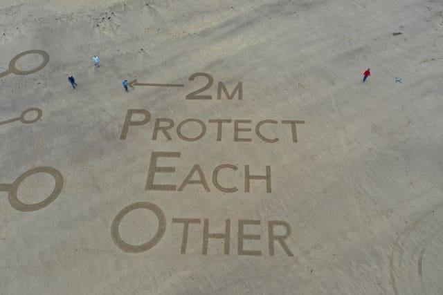 People walk across a giant piece of sand art which was created on the beach at Whitby, North Yorkshire (Richard McCarthy/PA)