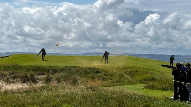 Greenkeeping staff blow away powdered paint from the 17th green