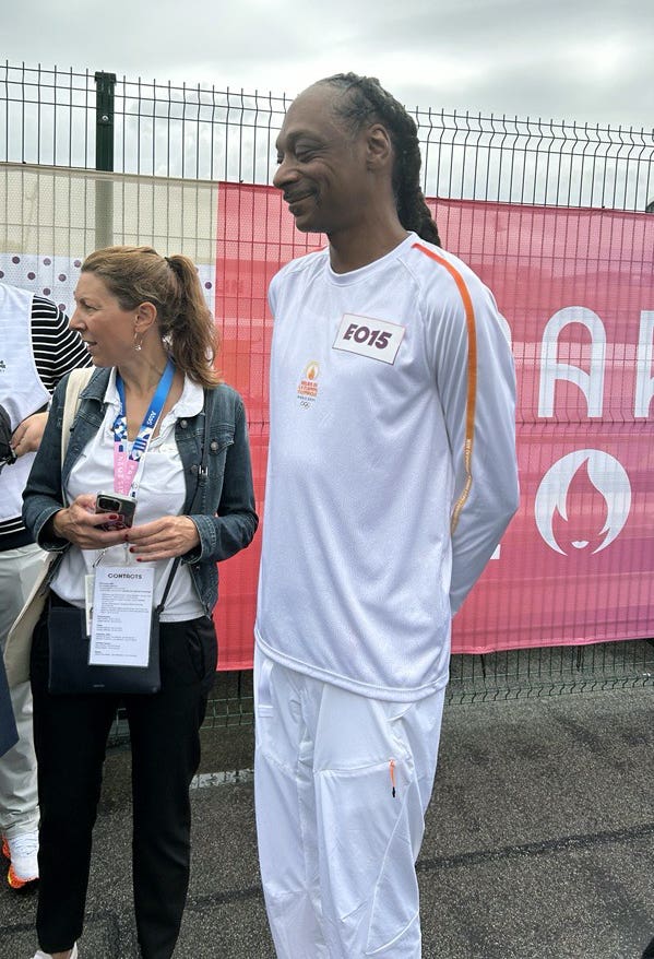 Snoop Dogg, dressed in white, smiles as he awaits the Olympic torch