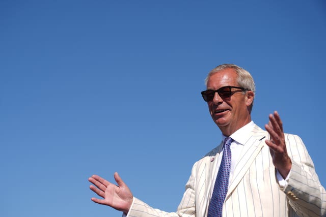 Nigel Farage, with his hands raised, under a blue sky