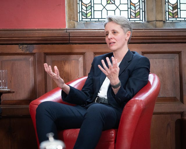 Professor Kathleen Stock gesturing with both hands while speaking, seated in a red armchair