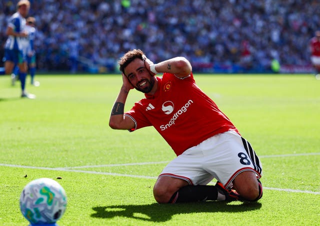 Manchester United’s Bruno Fernandes celebrates with a knee slide, with his hands over his ears, after scoring at Brighton