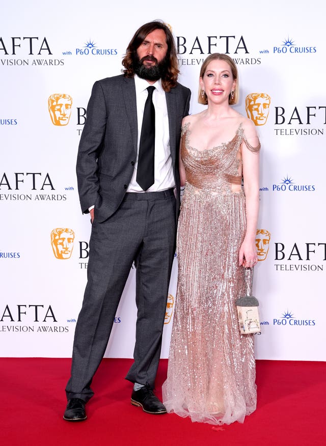 Joe Wilkinson in a suit and Katherine Ryan in a sparkly dress posing together at the 2024 Baftas