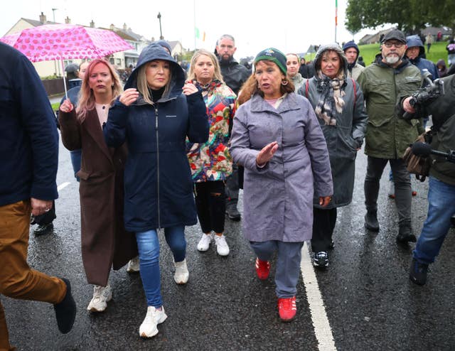 Michelle O'Neill and Mary Lou McDonald walking along a road in a crowd
