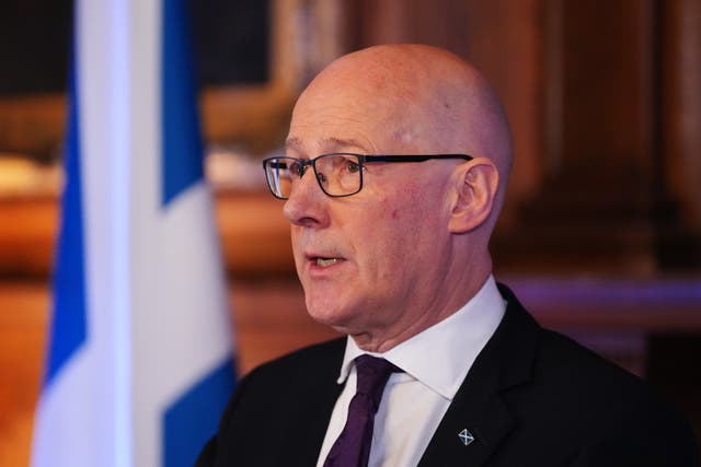 John Swinney speaking, with a Scottish flag in the background