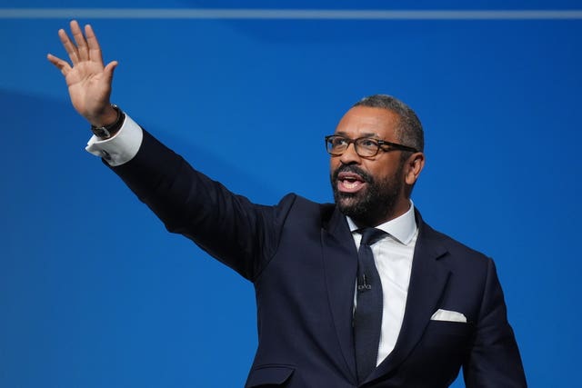 Sir James Cleverly waves to an audience