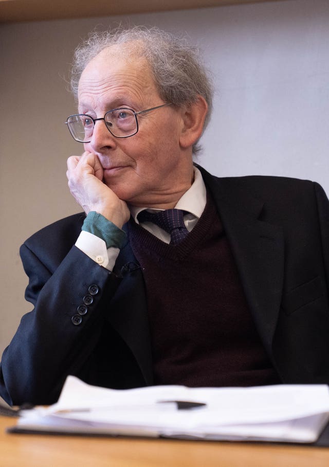 Sir David Natzler seated at a desk with one hand resting on his face