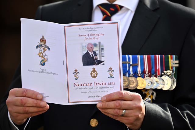 A man reads the order of service at the funeral of Norman Irwin