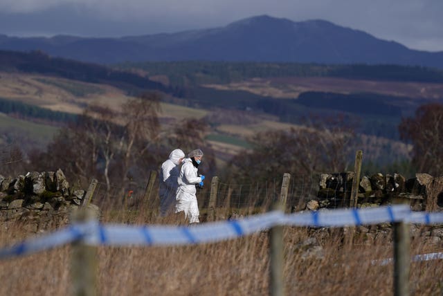 An officer in a white forensic suit within a rural area taped off with police tape
