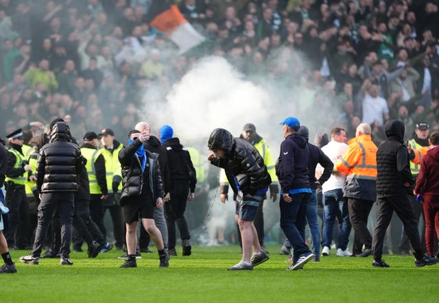 Fans and police on the pitch at Ibrox, with smoke from a flare visible