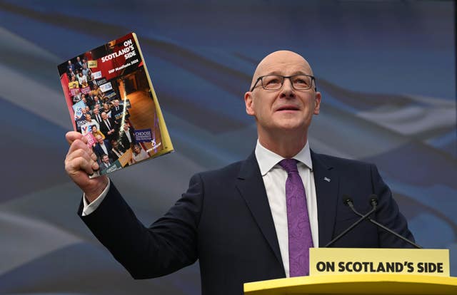 John Swinney speaking while holding up a copy of the SNP manifesto