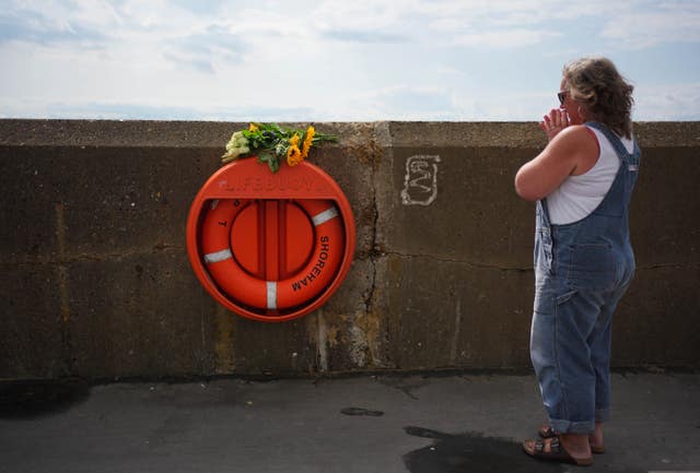 A woman places flowers on a lifebuoy at the beach in Shoreham-by-Sea