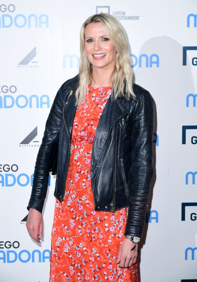 Jo Wilson, wearing red dress and black leather jacket, smiling at a red carpet event