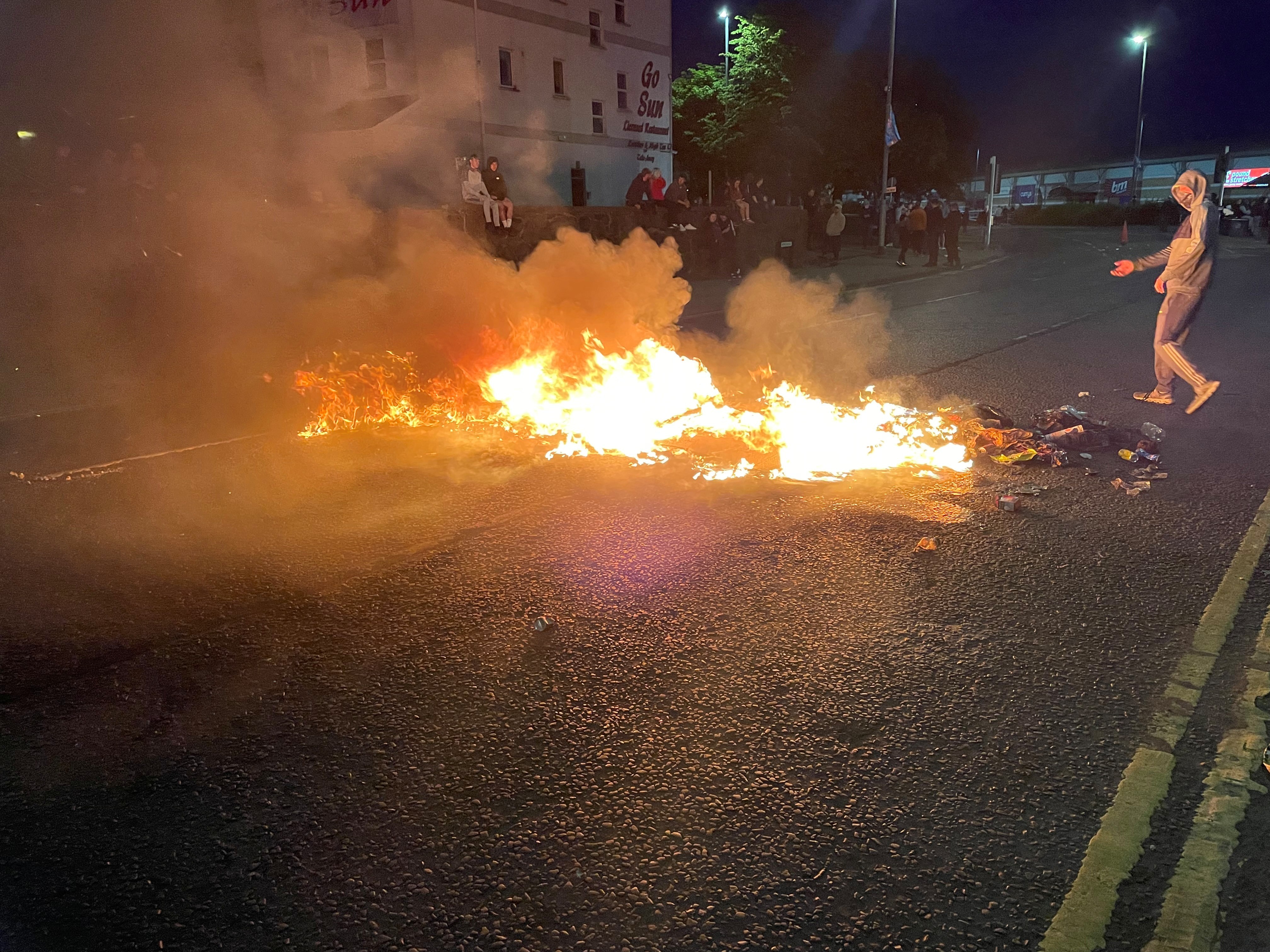 People watch debris on fire on a road