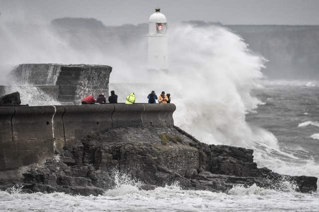 People watching waves crash against the harbour wall at Porthcawl, South Wales