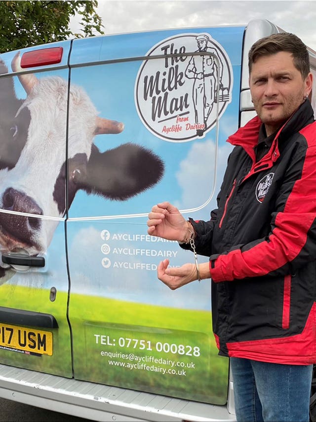 Russ Gibson, jokingly wearing handcuffs, after one of his milkmen was arrested on suspicion of being a burglar despite showing police pints of milk and empties in the back of his van