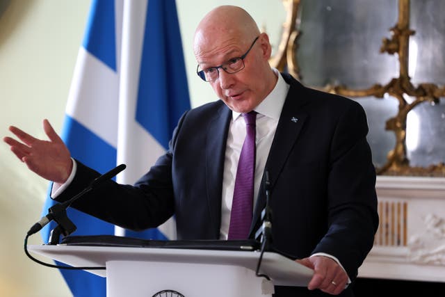 John Swinney gesturing with one hand while speaking from a lectern