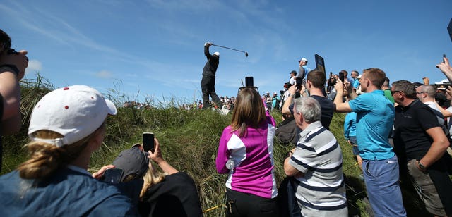 Spectators take photos of Woods as he tees off at the ninth hole at Portrush