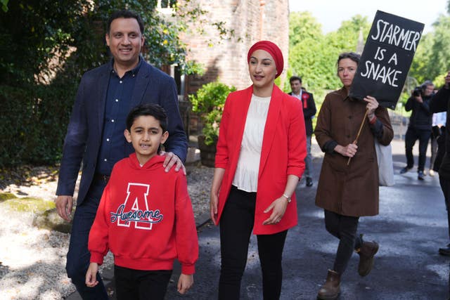 Anas Sarwar with son and wife, being followed by a protester holding a poster reading 'Starmer is a snake'