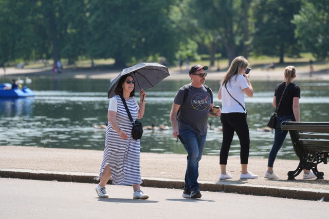 A woman shields from the sun under an umbrella while a man wears a baseball cap