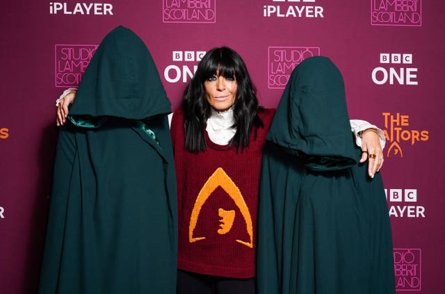 Claudia Winkleman with her arms round two hooded characters