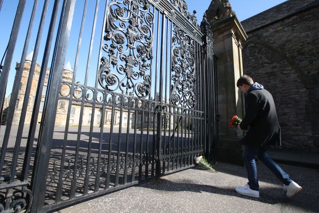 A man lays a floral tribute at the gates of the Palace of Holyroodhouse in Edinburgh (Andrew Milligan/PA)