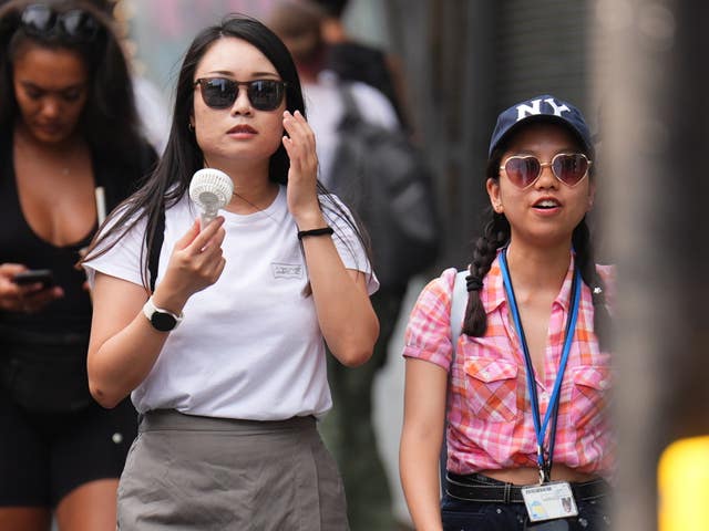 A person using a fan whilst walking in Leicester Square, central London 