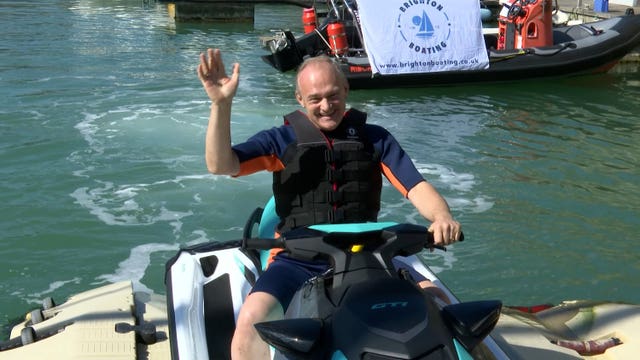 Sir Ed Davey waving while sitting on a jet ski