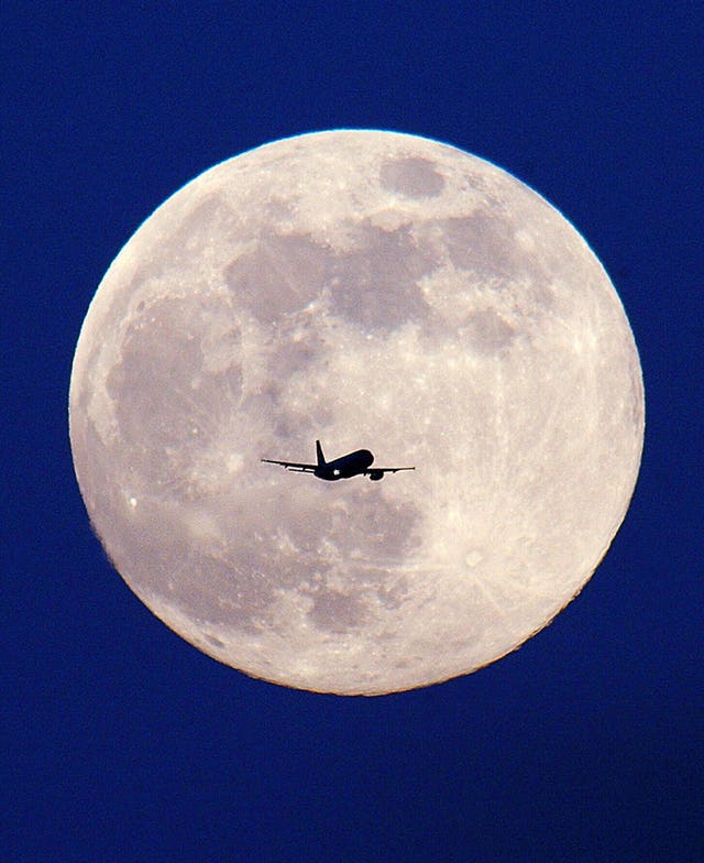 A passenger plane is silhouetted by the full moon  (Toby Melville/PA)