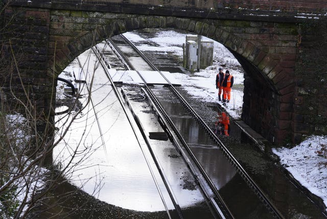 Two men in orange hi-vis stand beside a railway bridge looking at flooded tracks 