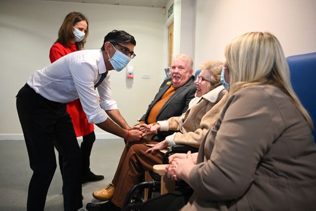 Mr Sunak, wearing a face mask, meets with a patient, centre, and her family during his visit to the Rutland Lodge Healthcare Centre in Leeds