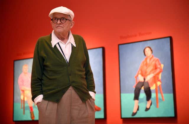 David Hockney standing in front of some of his artwork