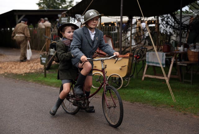 Two boys ride on a bike in Second World War era clothing