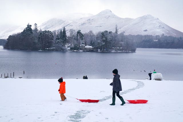 People pulling sledges in snowy conditions in Crow Park at Derwent Water near Keswick, Cumbria.