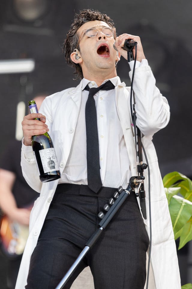 Matty Healy from The 1975 sings on stage holding a microphone and a bottle