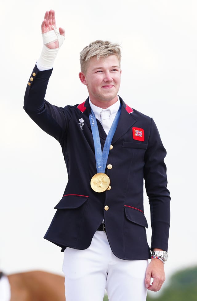 A smiling Harry Charles holds his right arm up to celebrate with his gold medal around his neck. 