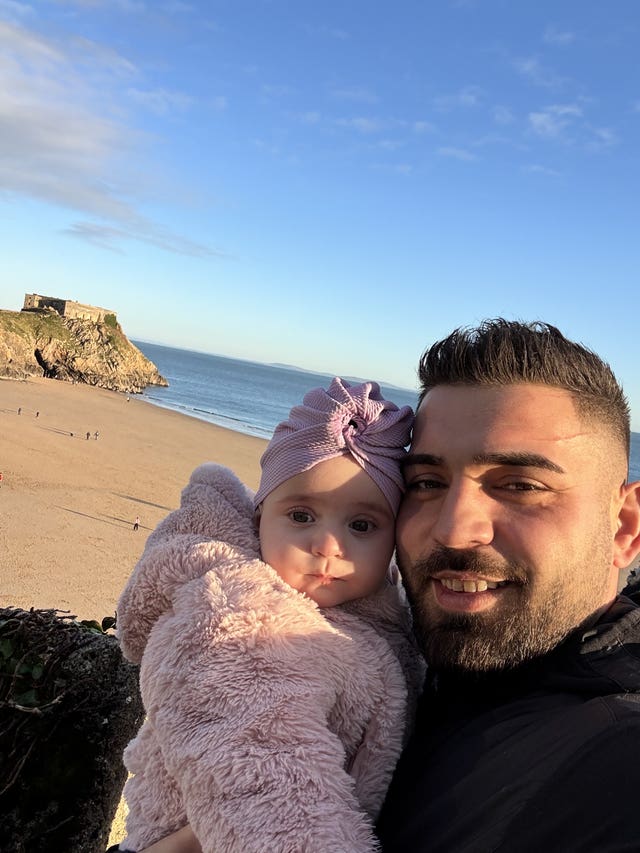 Sophia Kelemen in her father's arms with a beach in the background and blue skies